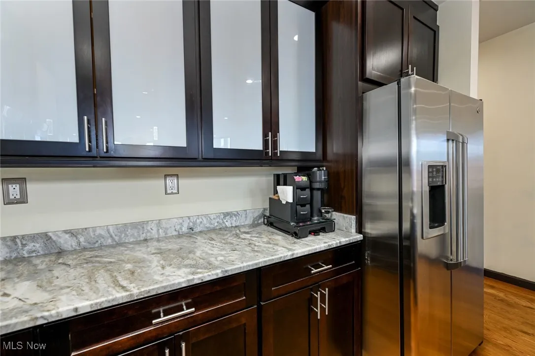 Kitchen with dark brown cabinetry, stainless steel refrigerator with ice dispenser, and glass insert cabinets