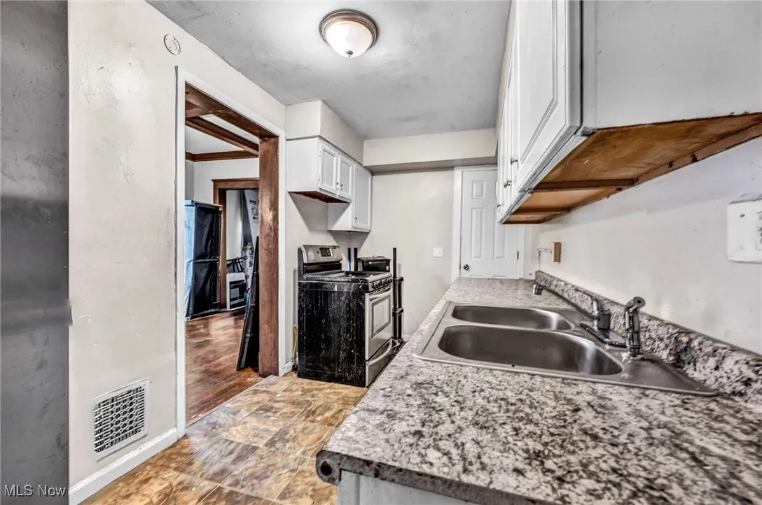 Kitchen with a sink, white cabinetry, gas range, baseboards, and visible vents
