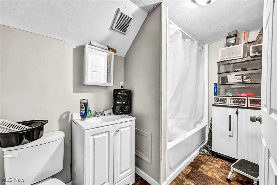 Bathroom featuring a textured ceiling, visible vents, stone finish floor, toilet, and lofted ceiling