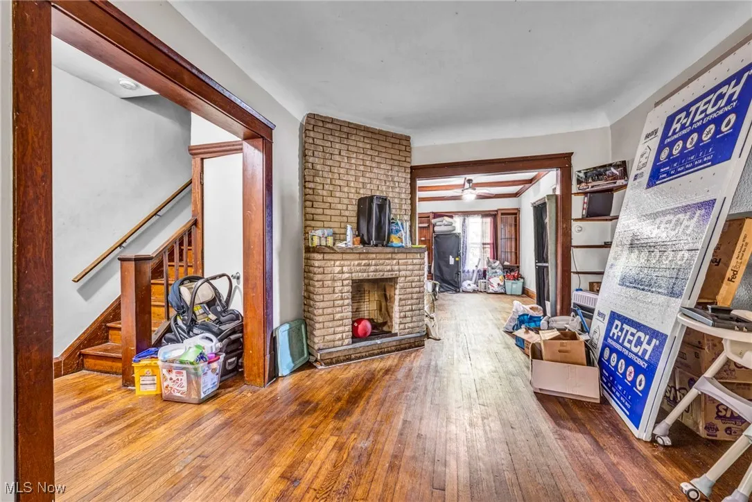 Living room with hardwood / wood-style floors, a ceiling fan, a brick fireplace, and stairway