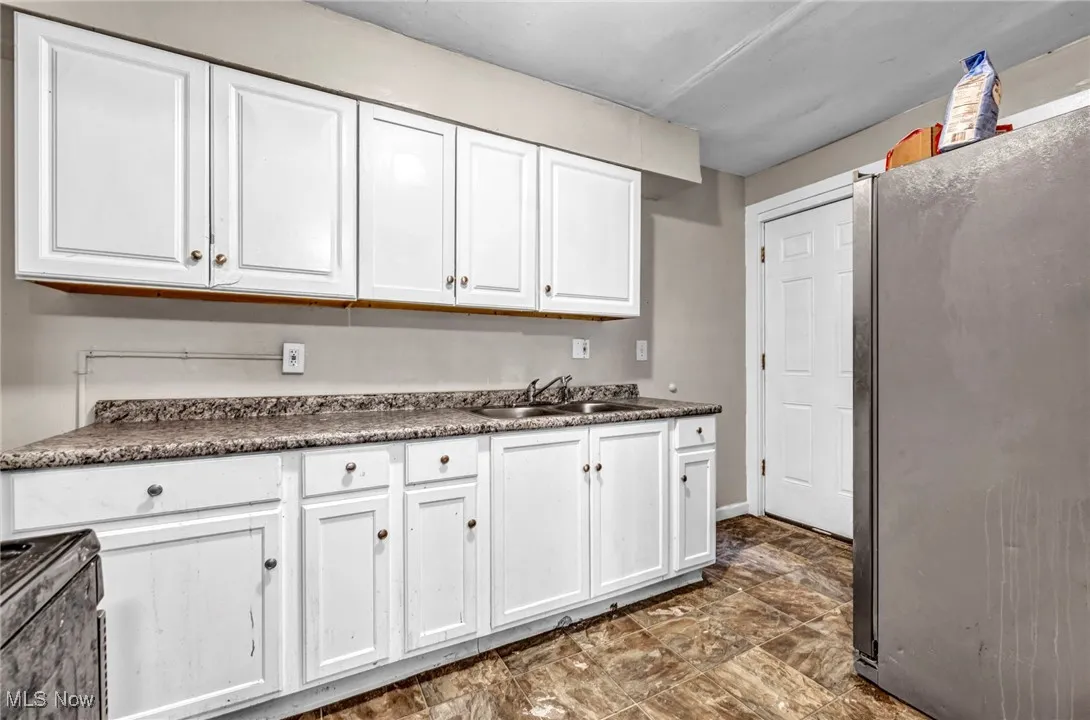 Kitchen with white cabinetry, range, a sink, dark countertops, and freestanding refrigerator
