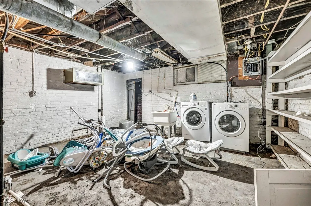 Washroom with washing machine and dryer, a sink, laundry area, and brick wall
