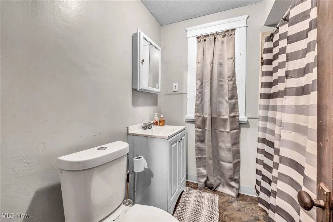 Full bath with baseboards, a shower with shower curtain, toilet, and vanity