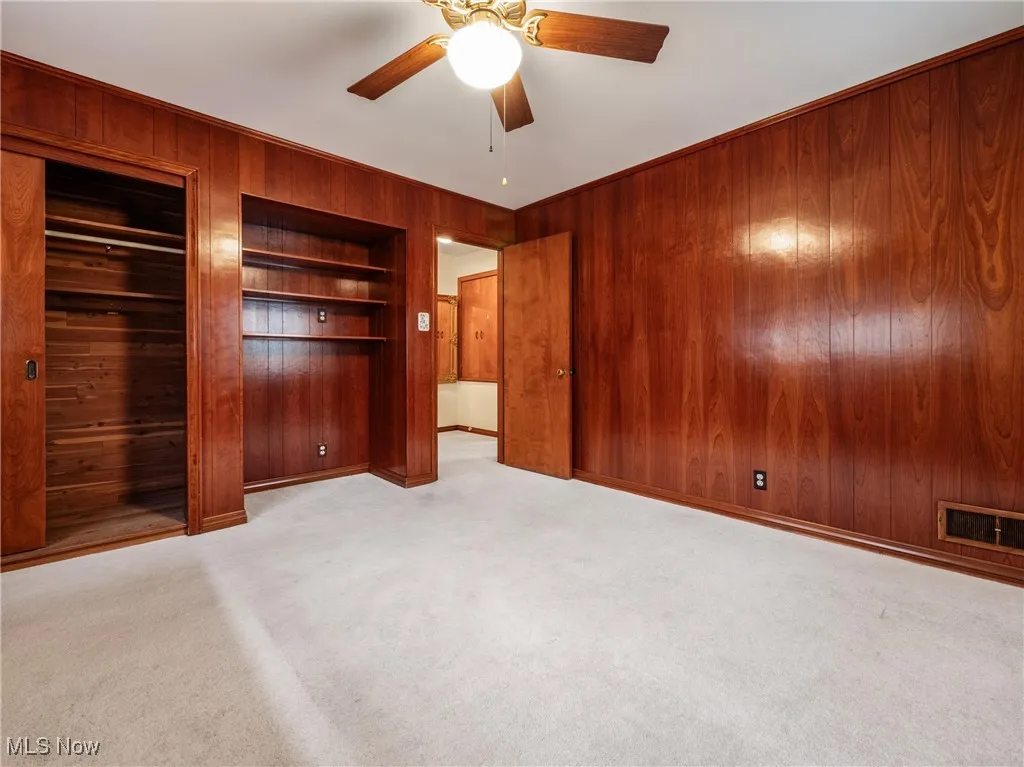 Unfurnished bedroom featuring wood walls, carpet flooring, visible vents, a ceiling fan, and a closet