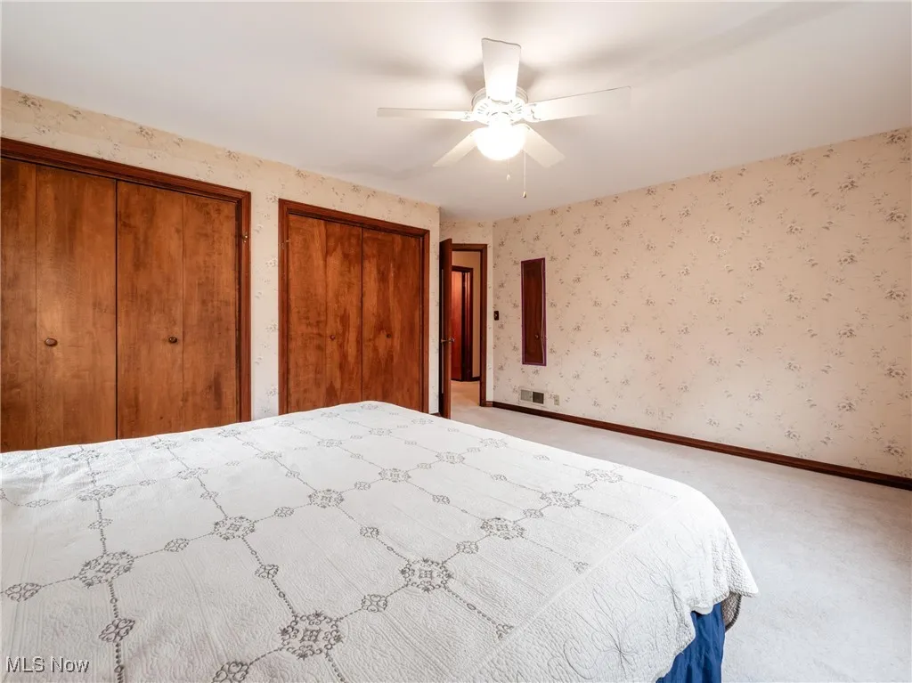 Unfurnished bedroom with baseboards, multiple closets, wallpapered walls, a ceiling fan, and light carpet