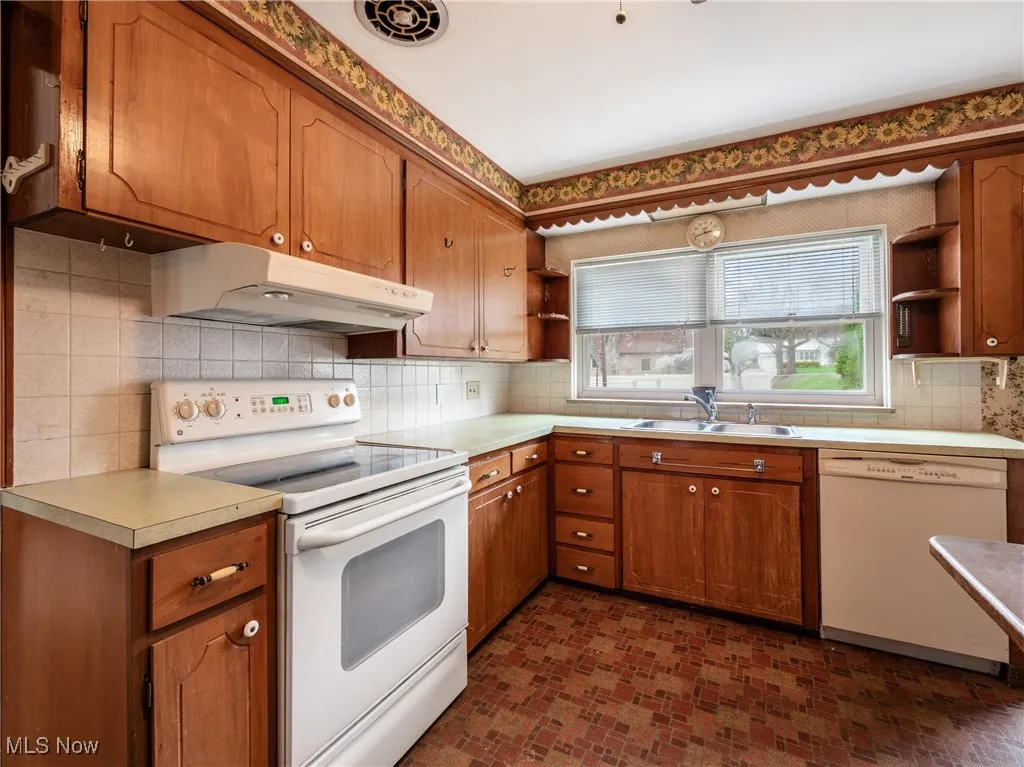 Kitchen featuring a sink, open shelves, brown cabinetry, under cabinet range hood, and white appliances