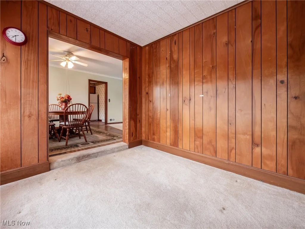 Carpeted spare room with baseboards, wooden walls, crown molding, and an ornate ceiling