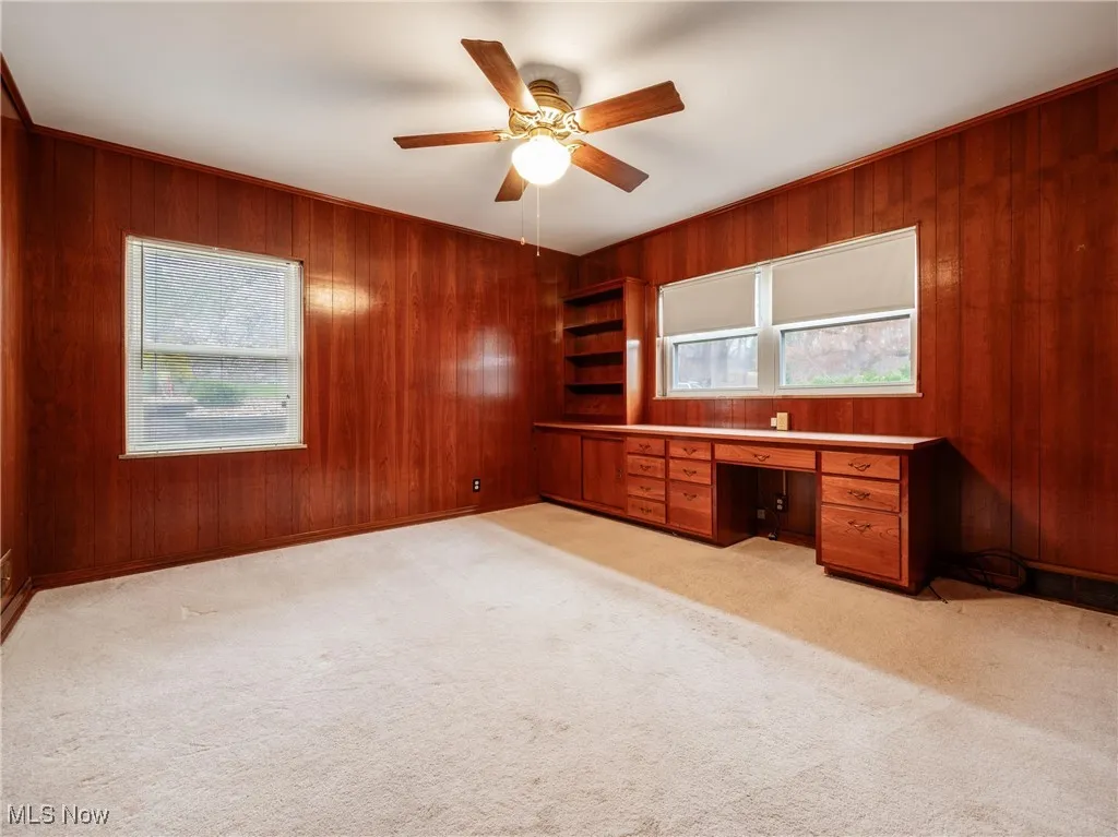 Unfurnished office with built in study area, ceiling fan, wooden walls, and light carpet