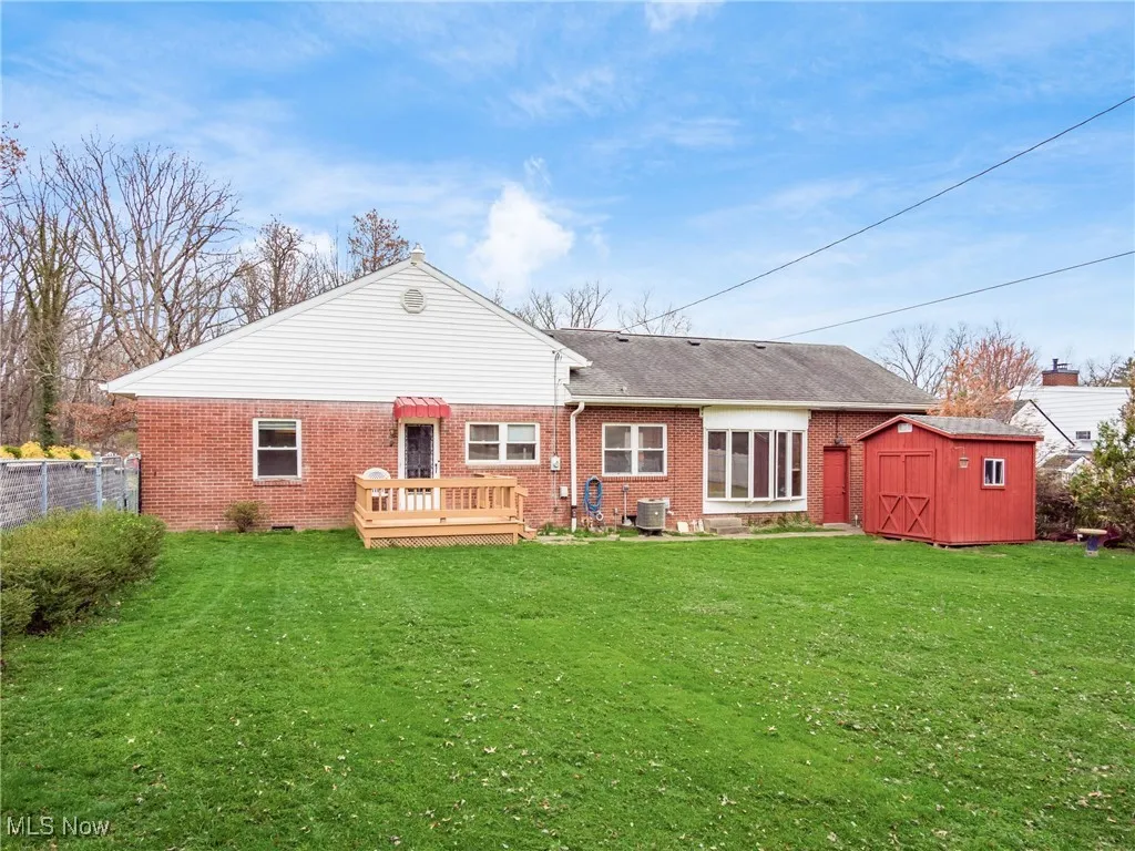 Rear view of house featuring a yard, brick siding, fence, and a storage shed