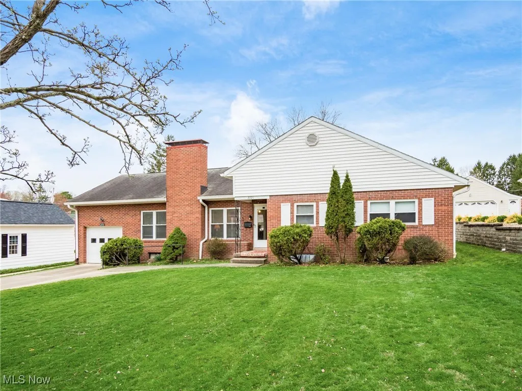 Ranch-style house featuring a front yard, concrete driveway, a chimney, an attached garage, and brick siding