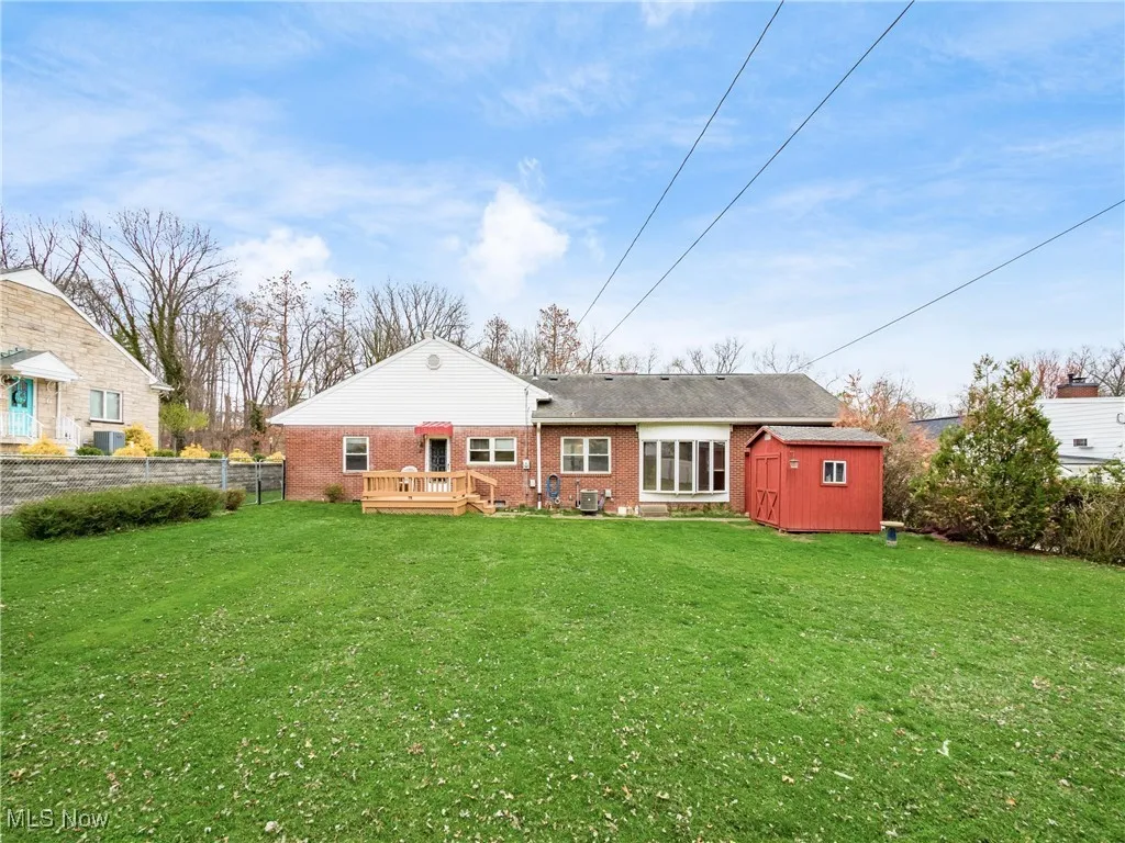 Back of property featuring an outbuilding, a shed, fence, a deck, and brick siding