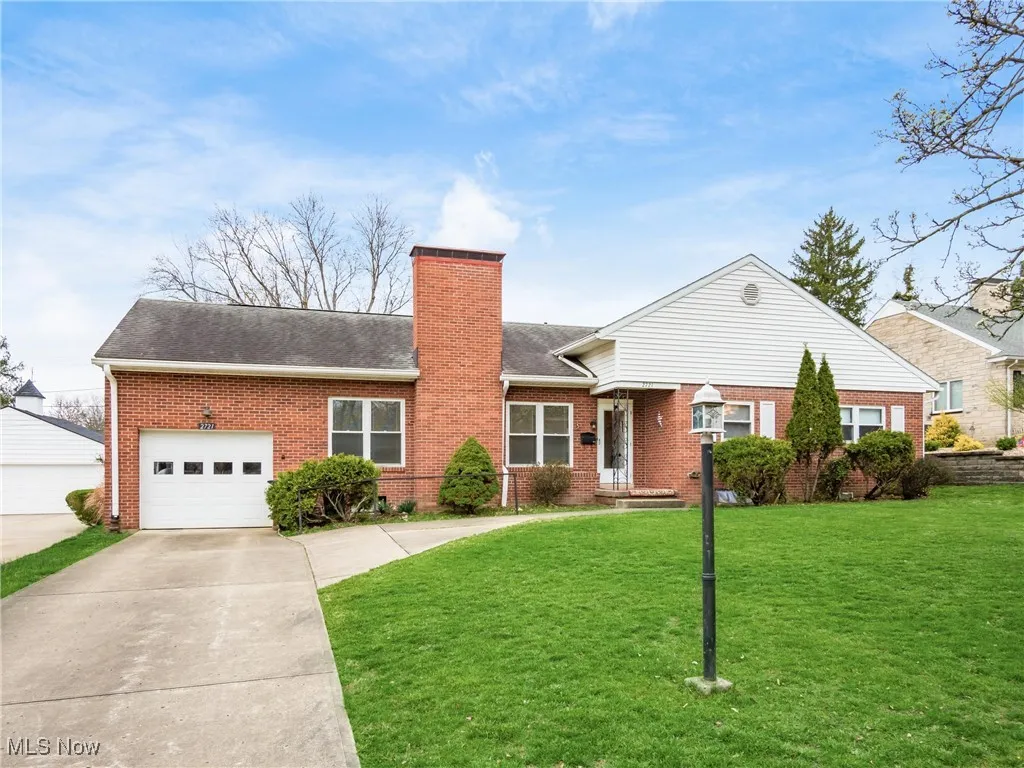 View of front of home featuring a chimney, an attached garage, a front yard, brick siding, and driveway