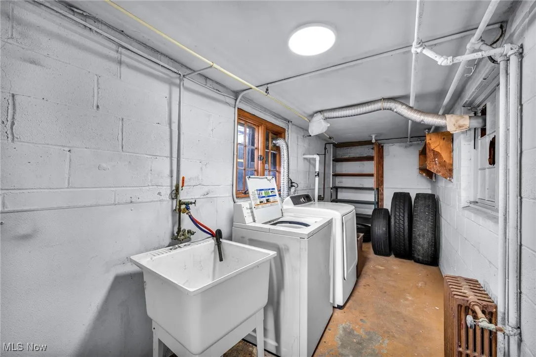 Clothes washing area featuring radiator heating unit, a sink, washing machine and dryer, and laundry area
