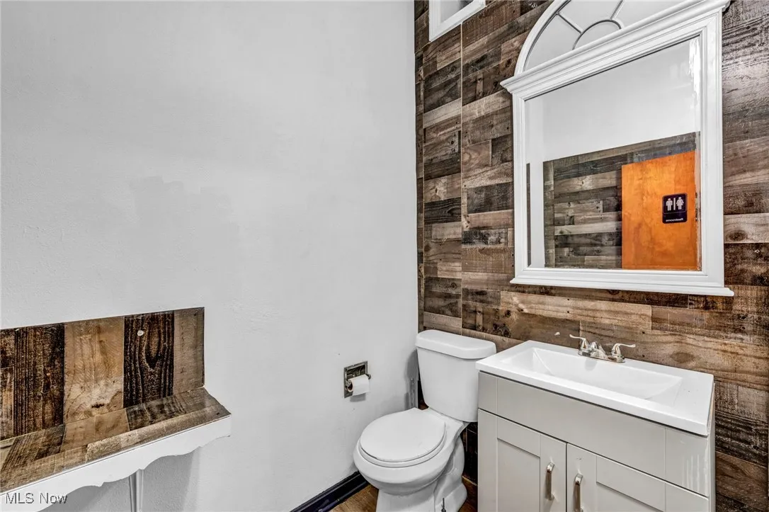 Bathroom featuring toilet, wood walls, and vanity
