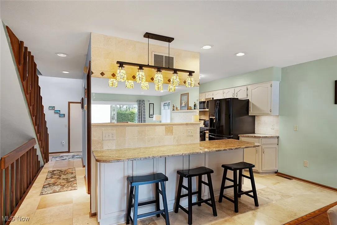 Kitchen with white cabinetry, a kitchen breakfast bar, black fridge with ice dispenser, decorative backsplash, and visible vents