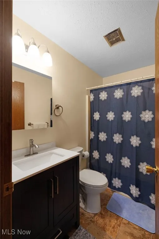 Bathroom with toilet, stone finish flooring, vanity, a textured ceiling, and visible vents