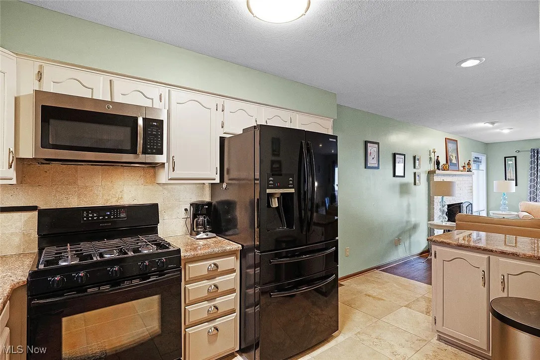 Kitchen with white cabinets, tasteful backsplash, a brick fireplace, baseboards, and black appliances