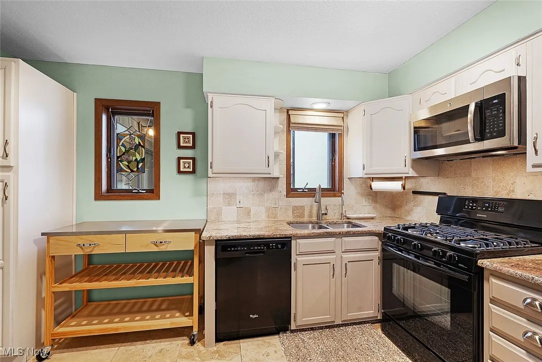 Kitchen with white cabinetry, a sink, tasteful backsplash, and black appliances
