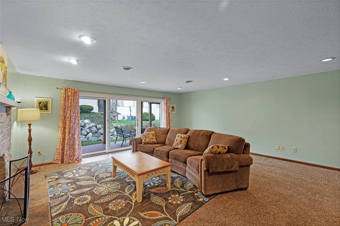 Living room featuring a textured ceiling, visible vents, baseboards, recessed lighting, and a stone fireplace