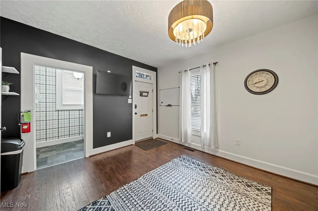 Entryway featuring wood finished floors, a textured ceiling, baseboards, visible vents, and an inviting chandelier