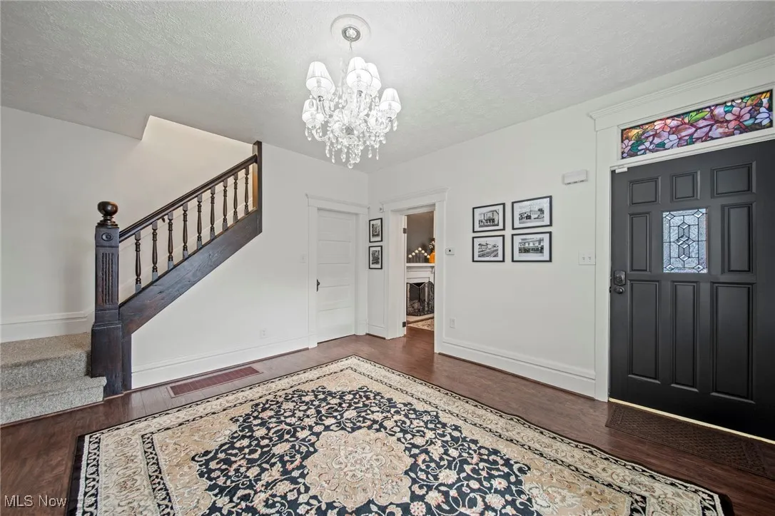 Foyer featuring a textured ceiling, wood finished floors, an inviting chandelier, and stairway