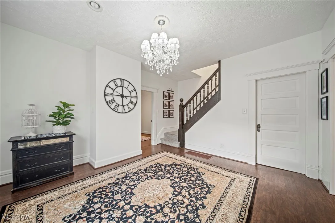 Entryway with stairway, a textured ceiling, visible vents, a notable chandelier, and wood finished floors