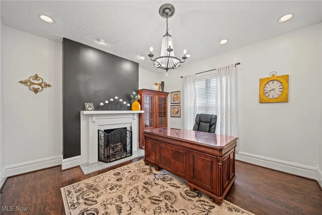 Home office with recessed lighting, an inviting chandelier, a fireplace with raised hearth, baseboards, and wood finished floors
