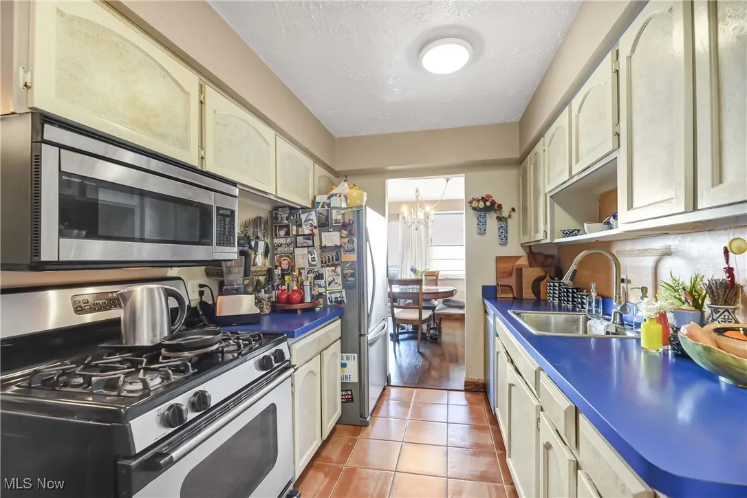 Kitchen with light tile patterned flooring, a sink, stainless steel appliances, dark countertops, and an inviting chandelier