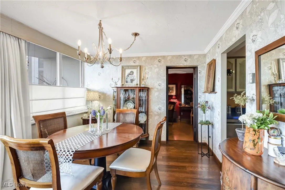 Dining area featuring crown molding, wallpapered walls, a notable chandelier, and wood finished floors