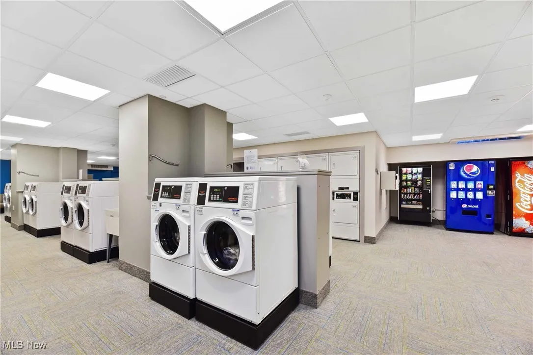 Community laundry room featuring visible vents, washer and clothes dryer, and light carpet