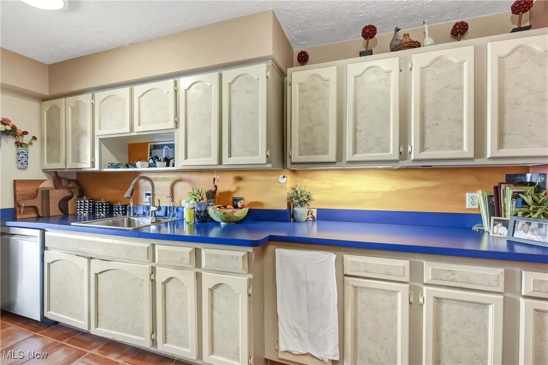 Kitchen with stainless steel dishwasher, tile patterned flooring, a sink, and a textured ceiling