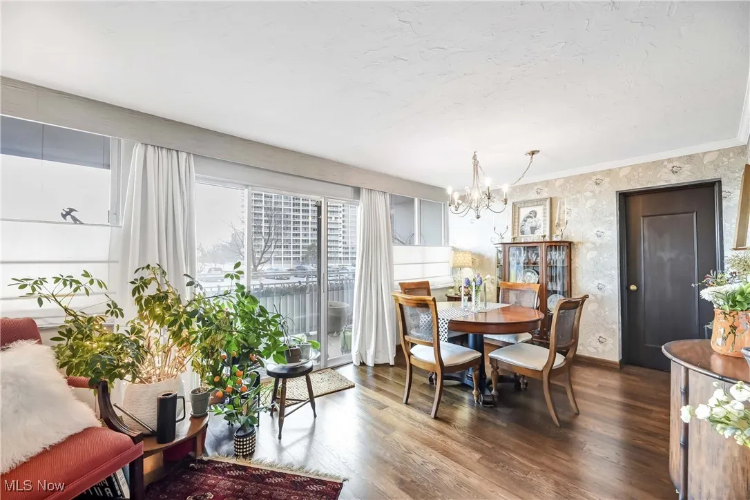 Dining area with dark wood-type flooring, crown molding, wallpapered walls, and a notable chandelier