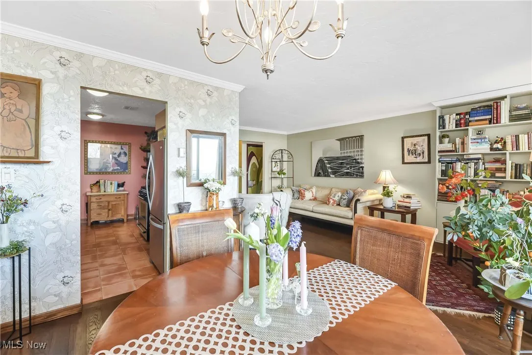 Dining space with an inviting chandelier, wallpapered walls, crown molding, and baseboards