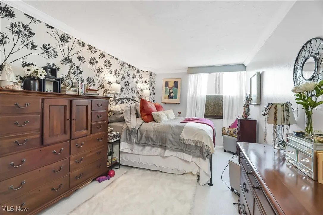 Bedroom with light carpet, wallpapered walls, and crown molding