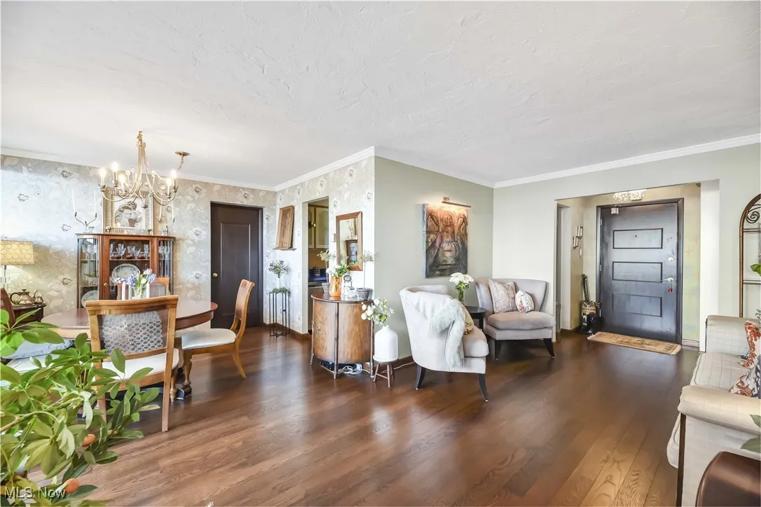 Living room with crown molding, a textured ceiling, wood finished floors, and a notable chandelier