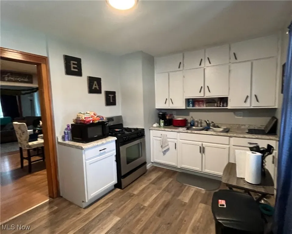 Kitchen with stainless steel gas range oven, a sink, dark wood-style floors, and black microwave
