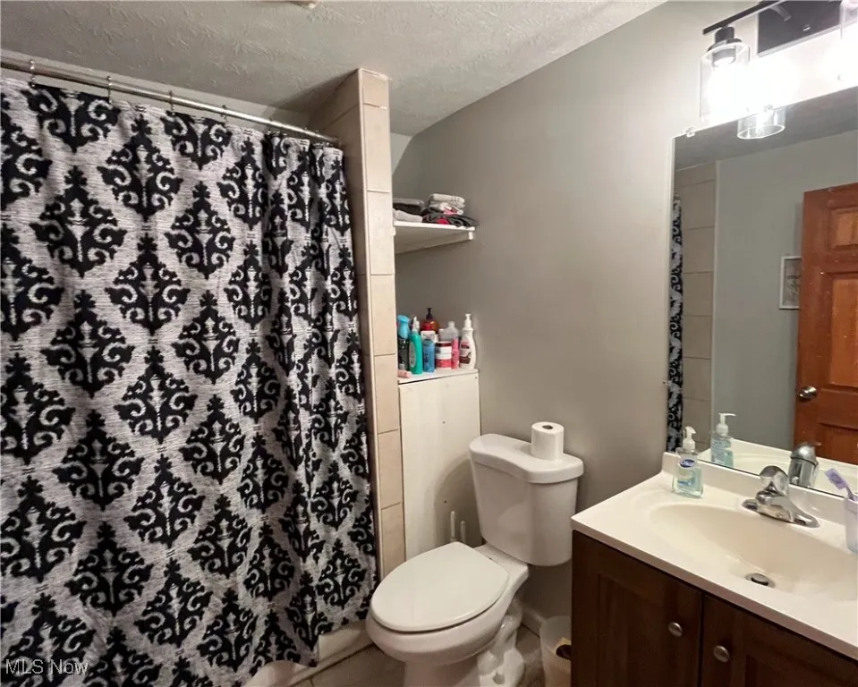 Full bathroom featuring curtained shower, toilet, vanity, and a textured ceiling