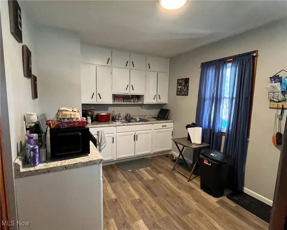 Kitchen with light countertops, white cabinets, a sink, black microwave, and dark wood-style floors