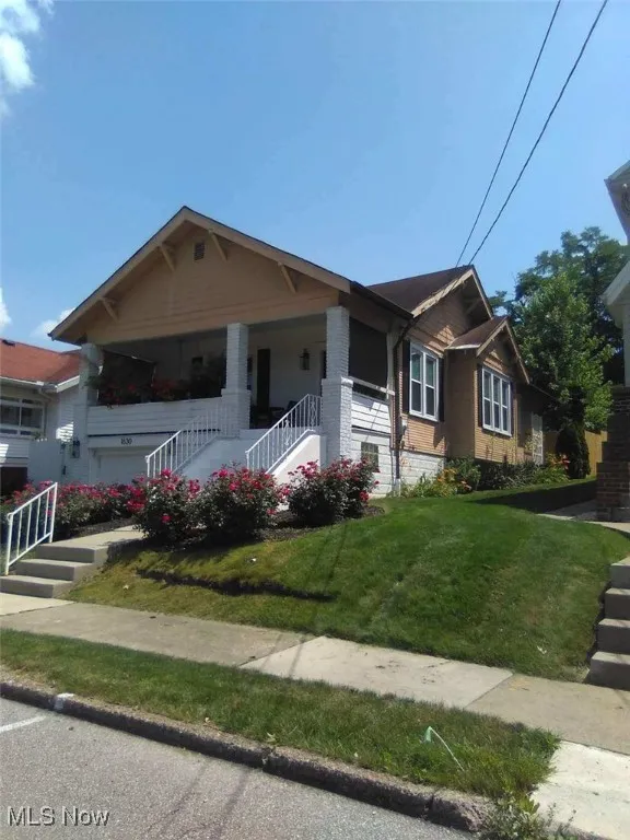 View of front of home featuring a front lawn, brick siding, stairs, and covered porch