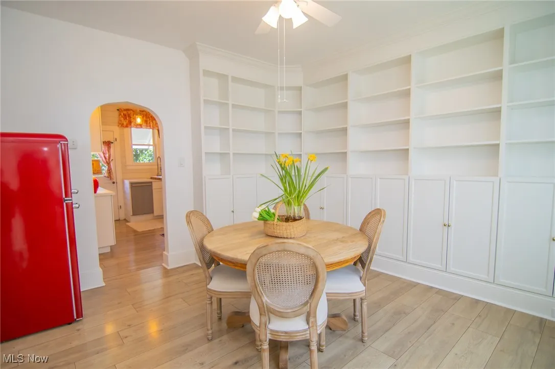 Dining room with light wood finished floors, crown molding, arched walkways, and ceiling fan