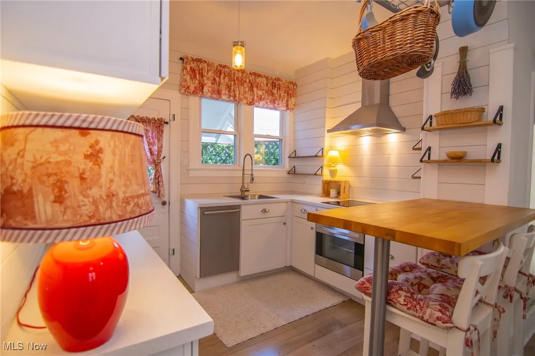Kitchen with stainless steel dishwasher, a sink, white cabinets, wall oven, and wall chimney exhaust hood