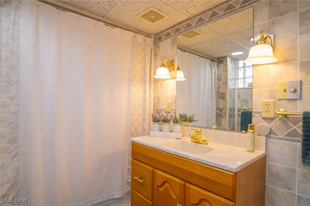 Bathroom with tile walls, visible vents, a paneled ceiling, and vanity