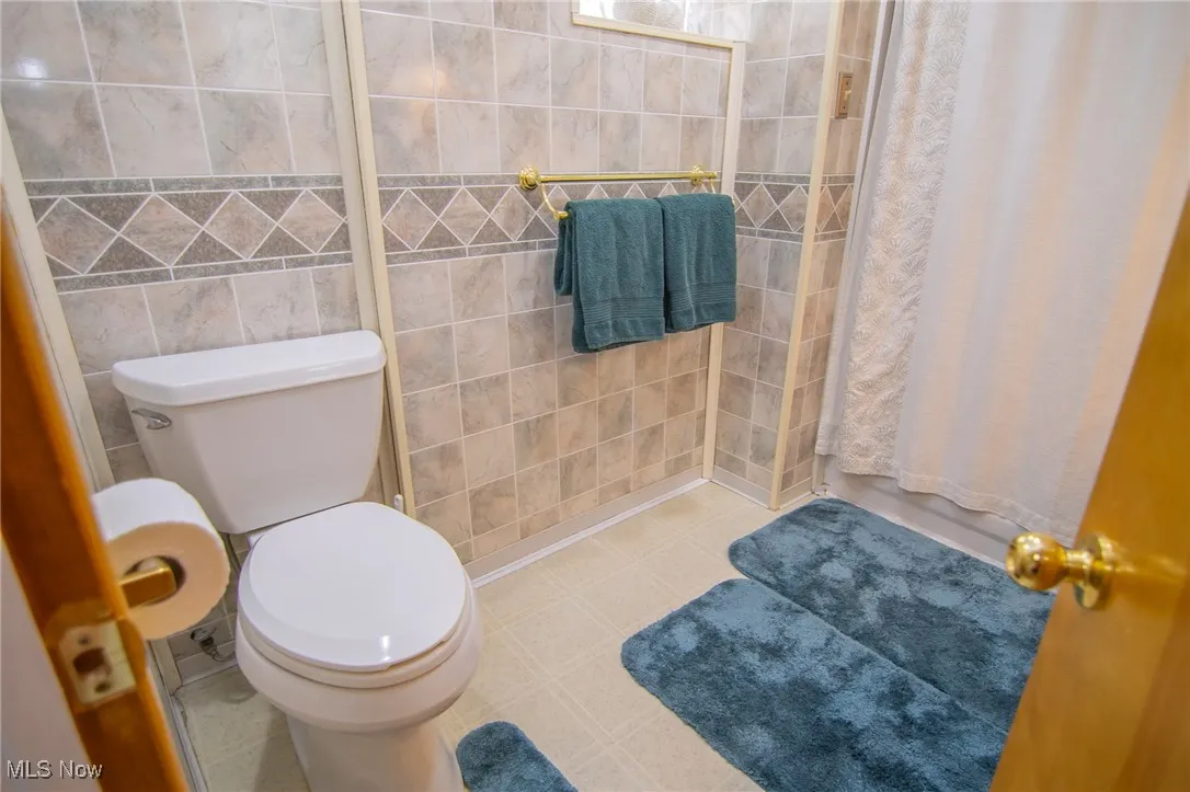 Bathroom with toilet, tile patterned flooring, and tile walls