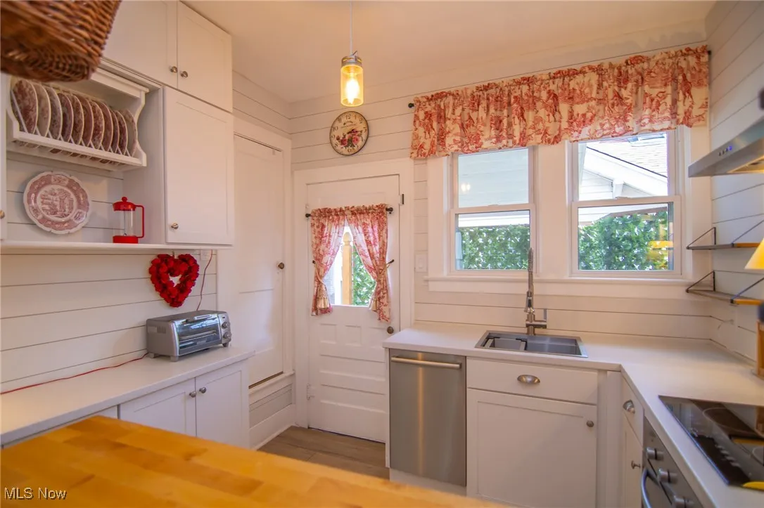 Kitchen with light countertops, a sink, open shelves, appliances with stainless steel finishes, and white cabinets