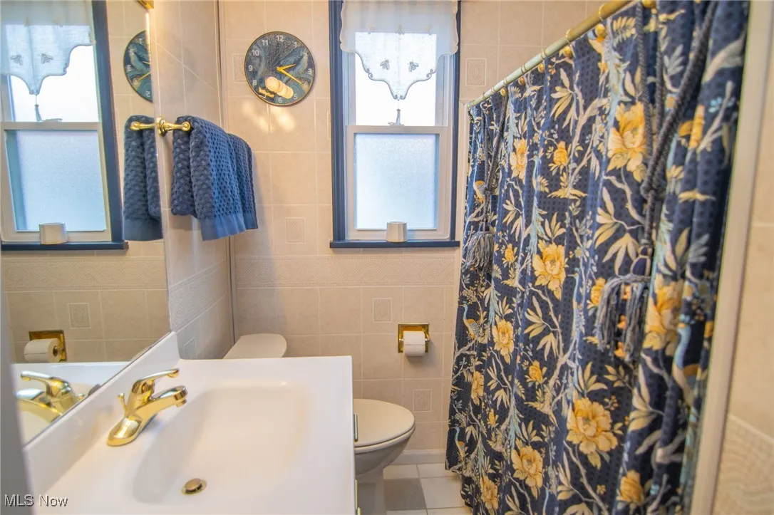 Full bath featuring toilet, a sink, tile patterned floors, and tile walls