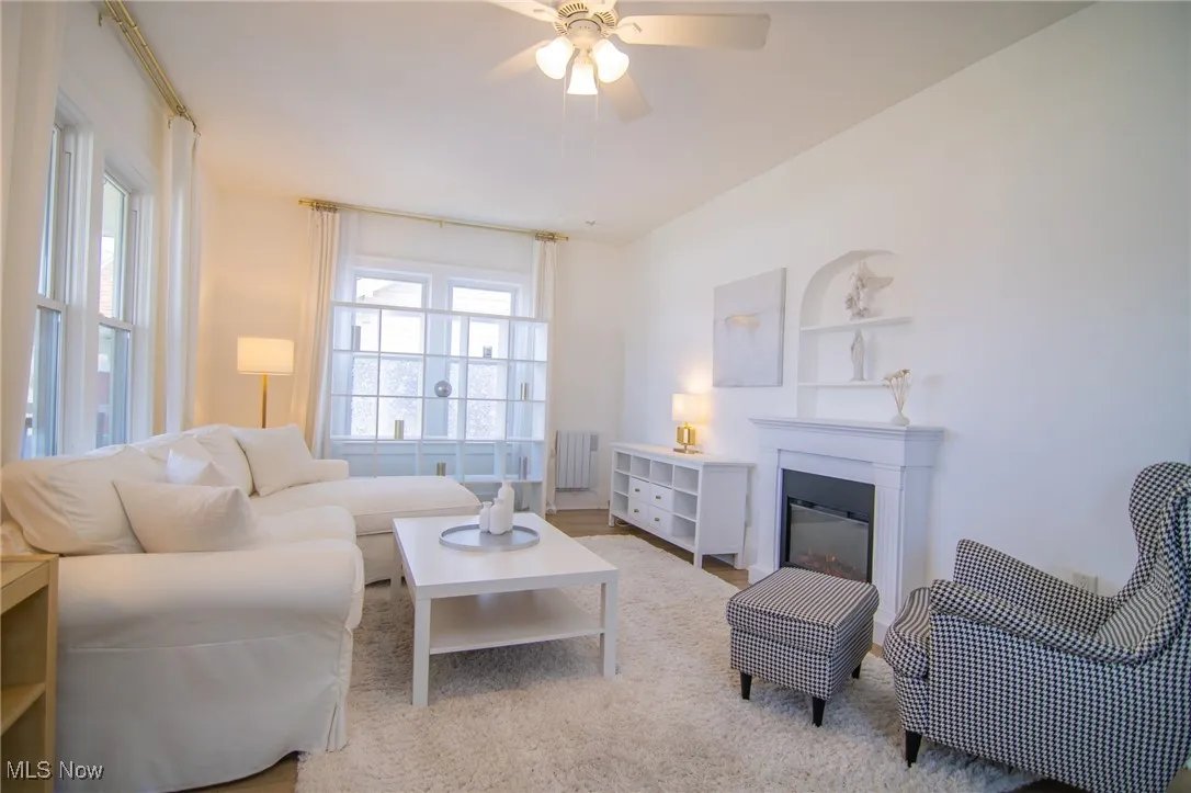 Living area with ceiling fan, a glass covered fireplace, and radiator heating unit