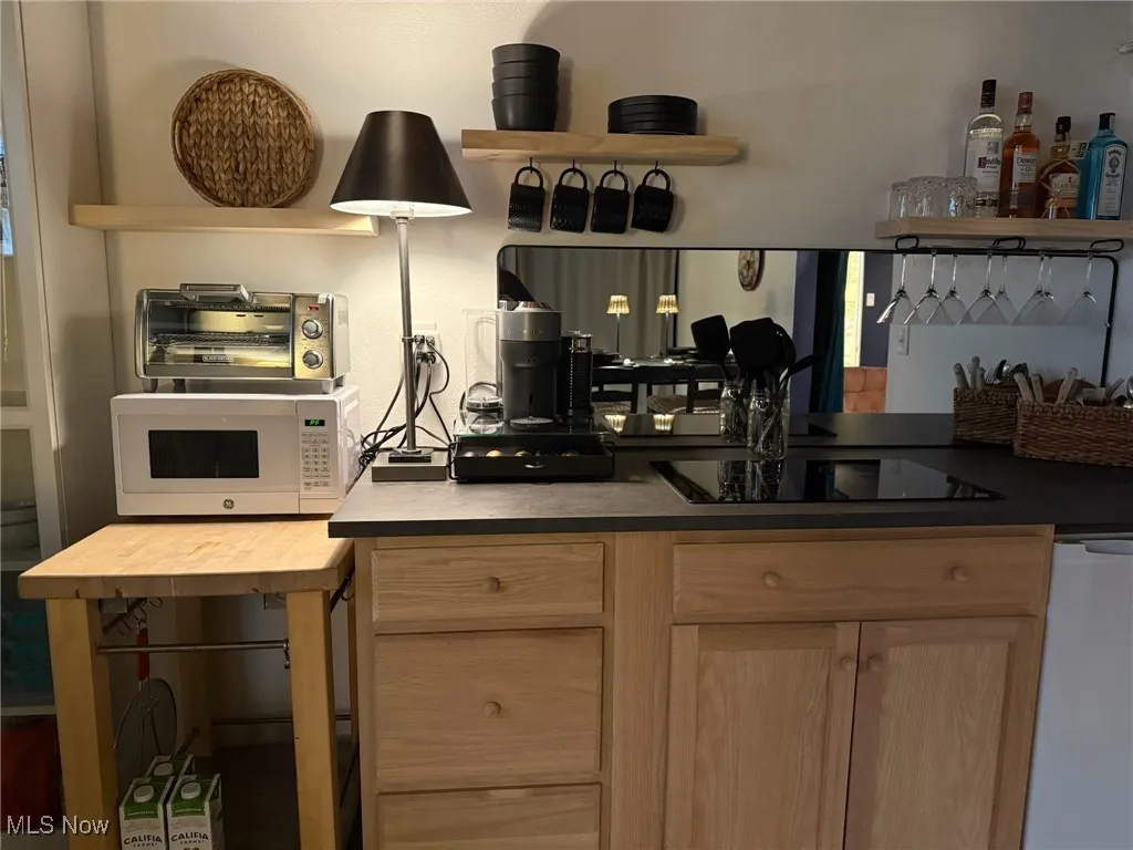 Kitchen featuring black electric stovetop, white microwave, light brown cabinetry, dishwasher, and open shelves