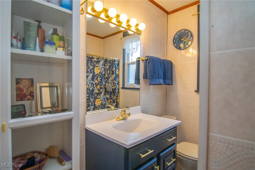 Full bathroom featuring tile walls, a shower with shower curtain, ornamental molding, toilet, and vanity
