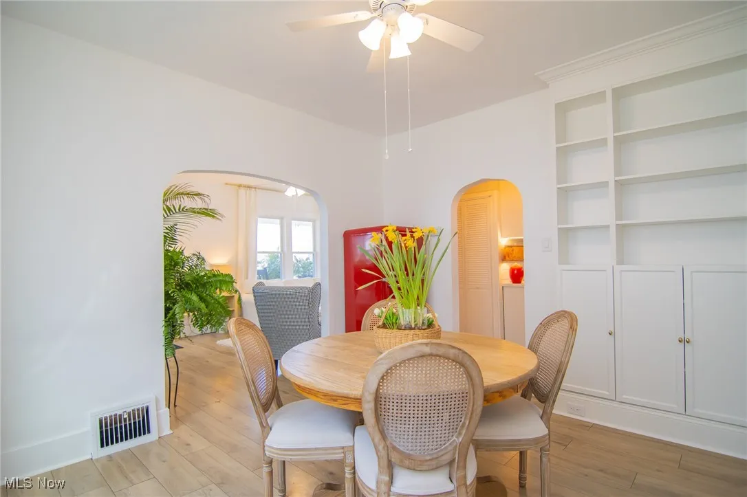 Dining area featuring baseboards, arched walkways, light wood-style floors, ceiling fan, and visible vents
