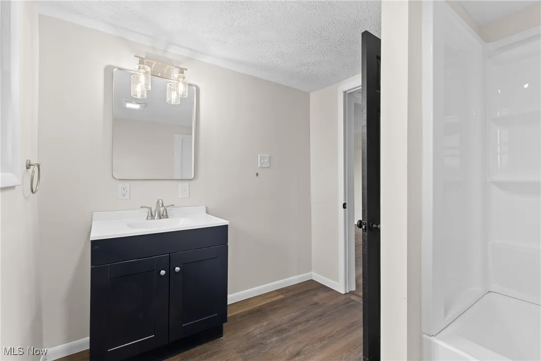 Full bath with a textured ceiling, baseboards, bathtub / shower combination, wood finished floors, and vanity